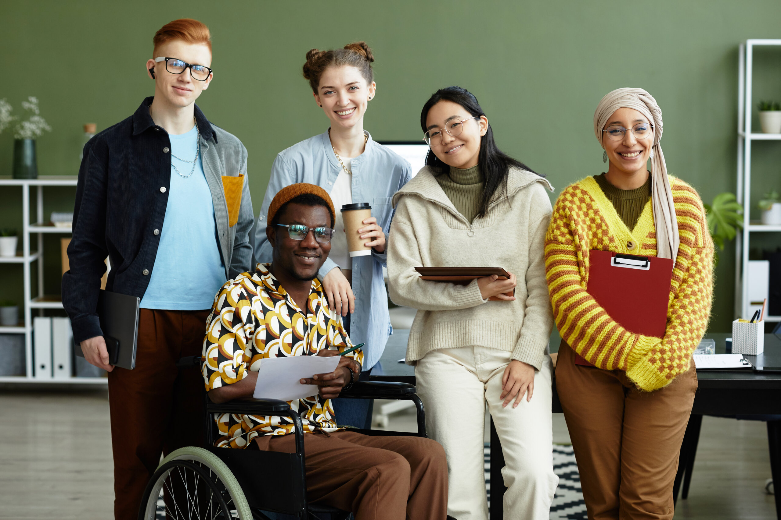 Portrait of diverse students looking at camera with cheerful smiles while posing in school, wheelchair user inclusion
