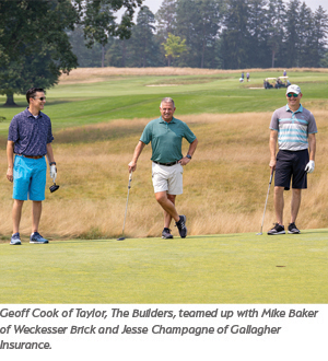 Three men stand on a golf green with clubs, engaged in conversation on a sunny day. They are dressed in golf attire and appear relaxed, with trees and a grassy field in the background.