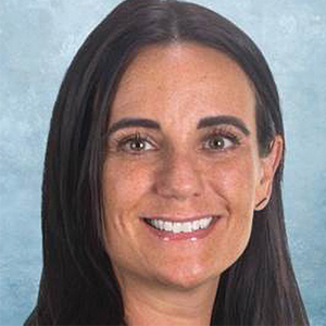 A woman with straight dark brown hair, arched eyebrows, and a bright smile poses in front of a light blue background.