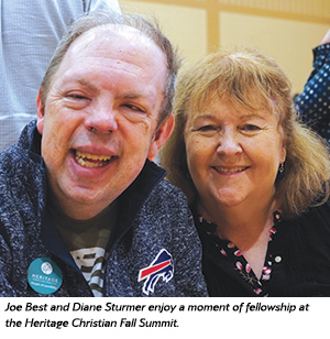 A man and a woman smiling and sitting close together, enjoying a moment of fellowship at an event. The man wears a Buffalo Bills jacket and the woman has shoulder-length hair.