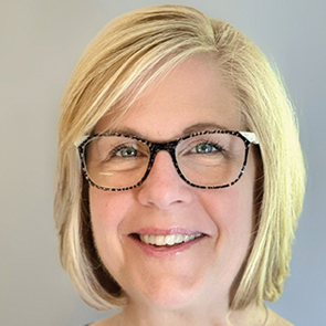A smiling woman with short, blonde hair and black-framed glasses, wearing light pink lipstick, in front of a plain light background.