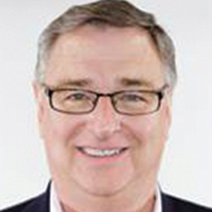 A middle-aged man with short brown hair, glasses, and a friendly smile is facing the camera. He is wearing a dark suit jacket and a light-colored shirt against a plain white background.