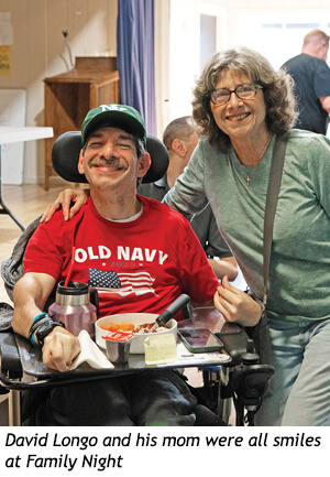 A smiling man in a wheelchair wearing an Old Navy t-shirt and a baseball cap posing with his smiling mother.