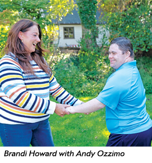 Brandi Howard and Andy Ozzimo hold hands and smile at each other while standing in a grassy yard.