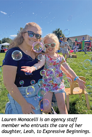 Lauren Monacelli and her daughter Leah posing for a photo outdoors surrounded by floating bubbles.